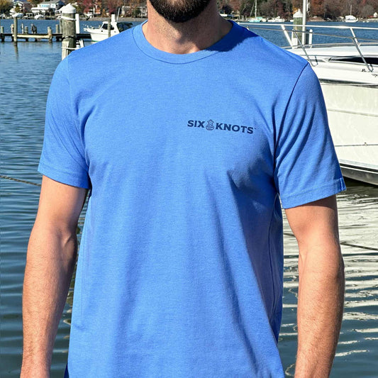 Man at a Maryland marina wearing the blue Six Knots Sink or Swim Classic T-Shirt. This lightweight, ultra-soft unisex tee is made from a breathable cotton-polyester blend and features a subtle Six Knots wordmark on the chest. Perfect for everyday wear, weekend relaxation, coastal getaways, casual outings, and easygoing waterfront style.