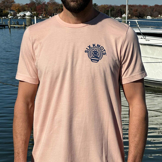 Man at a Maryland marina wearing the peach-colored Six Knots Perfect Day Classic T-Shirt. This ultra-soft, lightweight unisex tee is made from a breathable cotton-polyester blend and features a subtle Six Knots logo on the upper chest. Perfect for everyday wear, weekend relaxation, beach trips, coastal getaways, casual outings, and laid-back waterfront style.