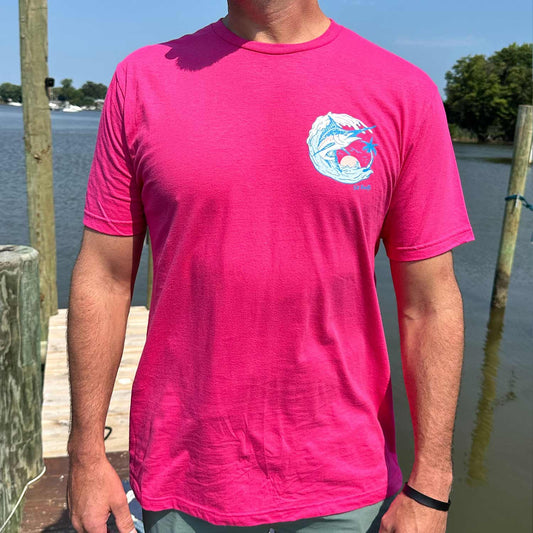 Man standing by the water wearing the Six Knots Summer Catch Classic T-Shirt in vibrant pink, featuring a subtle front chest badge with a marlin leaping from the water. This lightweight, ultra-soft unisex cotton-polyester blend tee delivers breathable, all-day comfort — ideal for everyday wear, weekend lounging, travel days, casual outings, tropical beach mornings, and relaxed seaside layering..