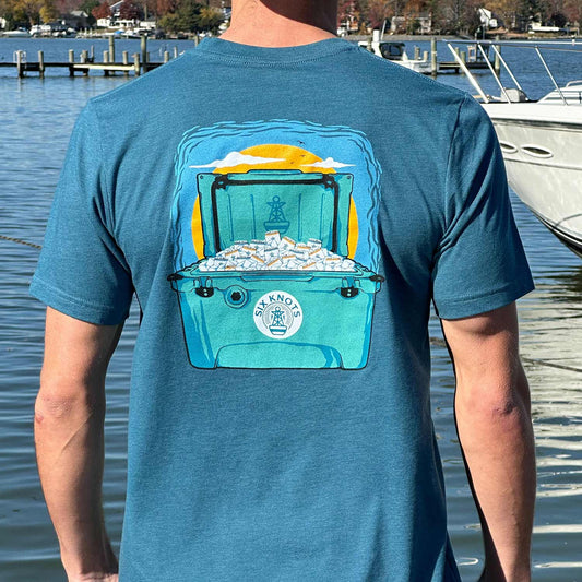 Rear view of a man at a Maryland marina wearing a deep teal Six Knots Weekender Classic T-Shirt. This lightweight, ultra-soft unisex tee is made from a breathable cotton-polyester blend and features a bold graphic of a sunset-lit cooler filled with seltzers. Perfect for casual weekends, beach trips, coastal getaways, relaxed outdoor gatherings, and everyday warm-weather wear.