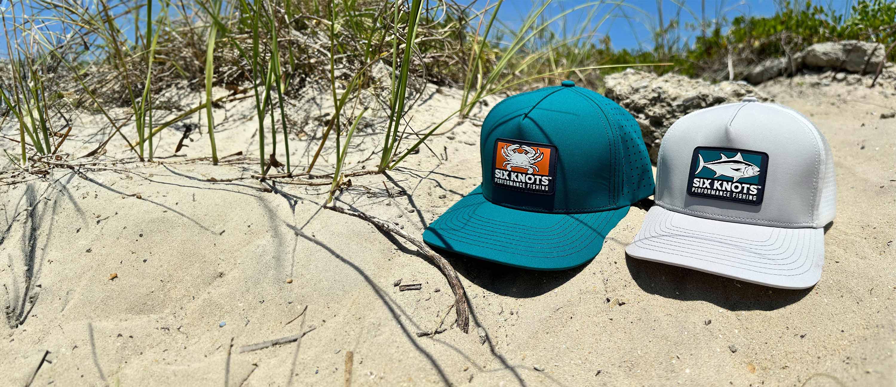 Six Knots water-resistant snapback hats resting on sandy beach in North Carolina – durable boating hats for sun and surf conditions