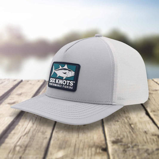 Angled side view of the Six Knots Tuna Chaser Snapback Hat on a dock with a blurred marina backdrop. This premium gray fishing hat is water-resistant and features a bold embroidered patch with a tuna graphic and 'Six Knots Performance Fishing' branding. Built for durability, breathability, and sun protection, it's ideal for offshore fishing, boating, beach days, and rugged coastal adventures.